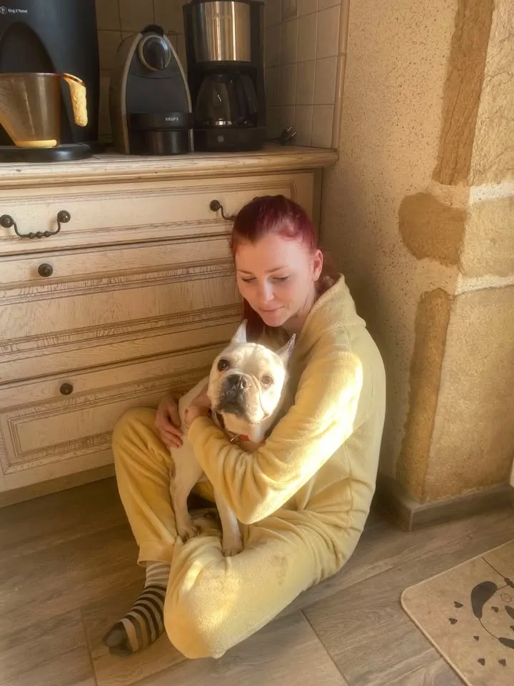 Candice, assise par terre dans la maison, tient un bouledogue blanc dans ses bras.