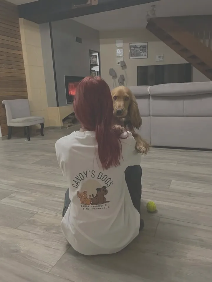 Candice, de dos, assise sur le sol d'un salon, tient un cocker dans ses bras.